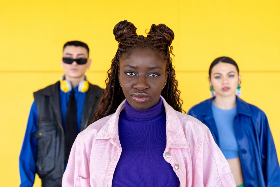 A young Black woman with braided hair leads a diverse group of friends against a yellow background.
