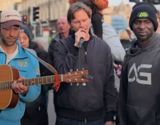 Street performer singing and playing guitar with a crowd watching.