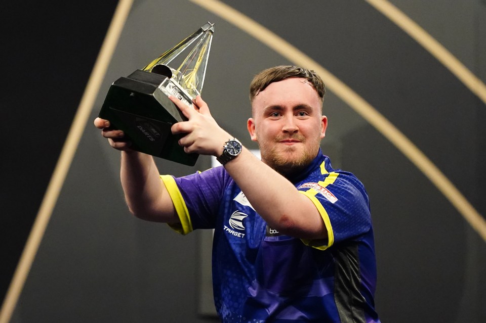 Luke Littler holding a darts trophy.