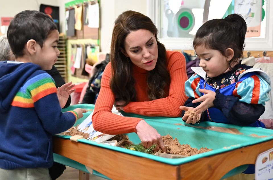 The Princess of Wales playing with children in a sandpit at a nursery school.