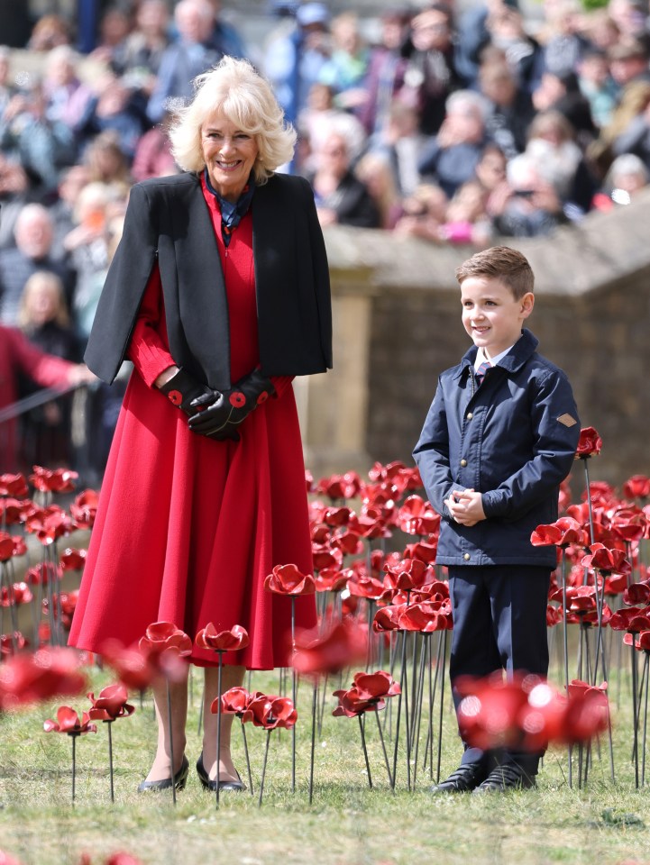 Queen Camilla with a child amidst a ceramic poppy display at the Tower of London, commemorating the 80th anniversary of VE Day.