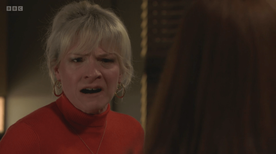 Screenshot of a woman in a red turtleneck, looking distressed.