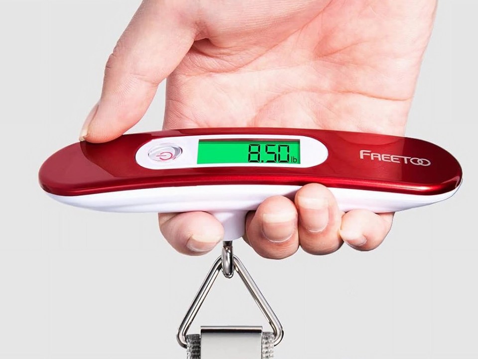 Hand holding a red and white digital luggage scale showing a weight of 8.50 lb.