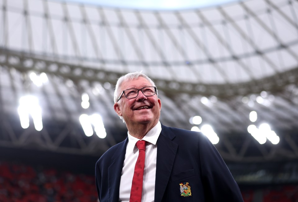 Sir Alex Ferguson smiling at a stadium.