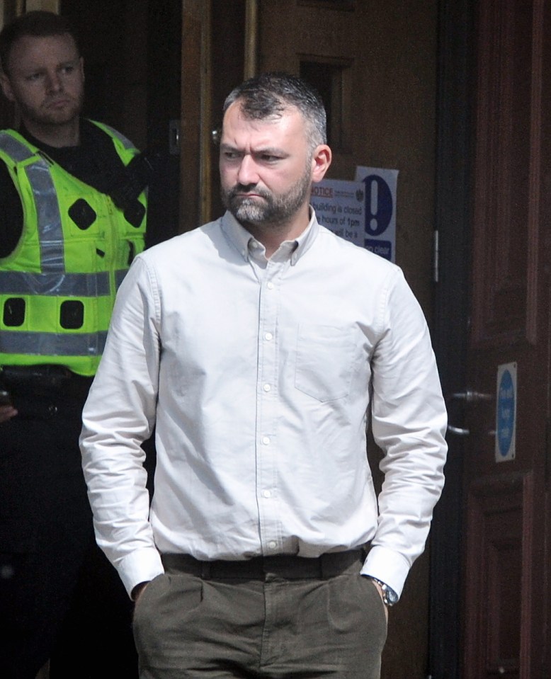 Man in light shirt and dark trousers standing outside a building.