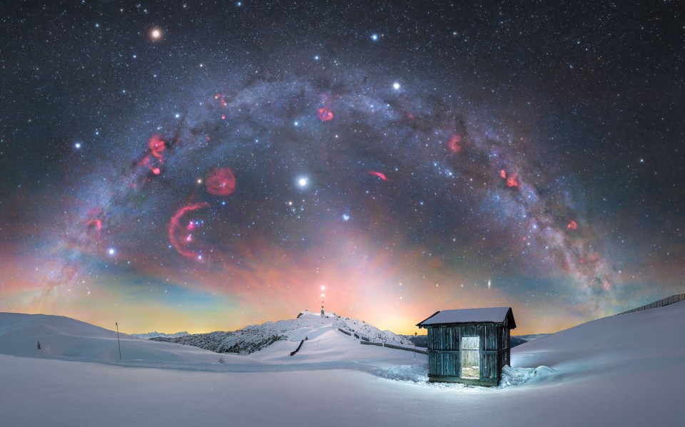 Winter Milky Way over Dobratsch Mountain, Austria, with a small cabin in the foreground.