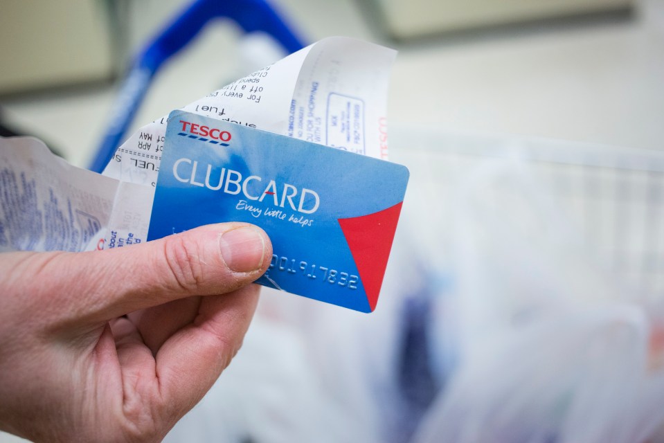 A hand holding a Tesco Clubcard and a receipt.