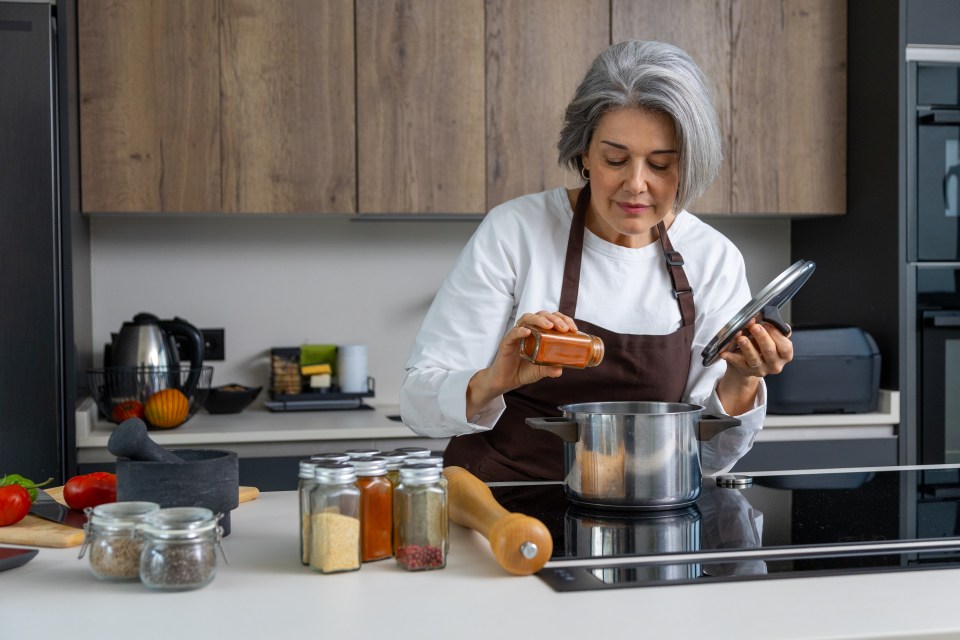 A mature woman seasoning food in a modern kitchen.