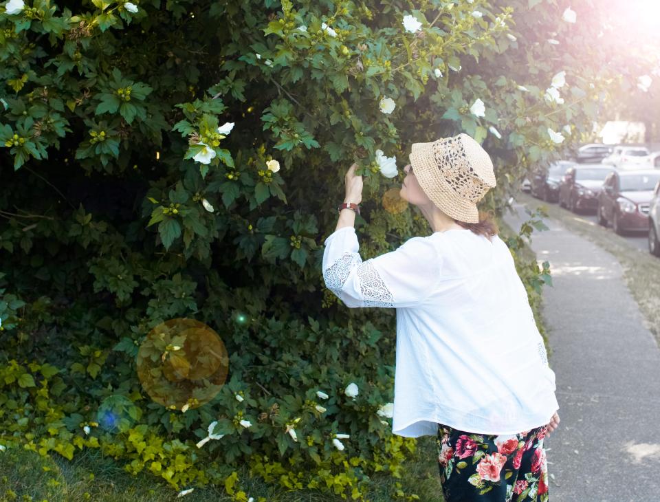 Woman smelling white flowers on a bush.
