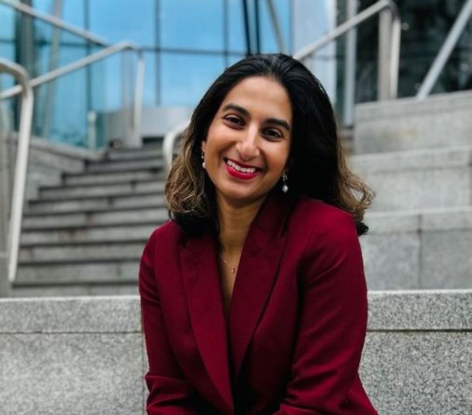 Woman in a red blazer smiling outdoors.