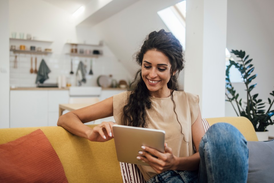 Smiling woman using a tablet on a sofa.