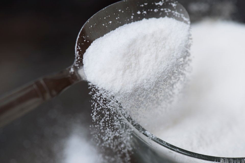 Sugar pouring from a spoon into a bowl.