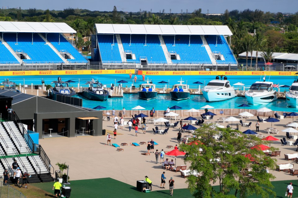 Overview of a Formula 1 Miami Grand Prix fan zone with bleachers, boats in a pool, and people relaxing.