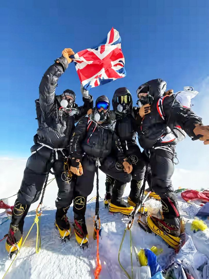 Four British climbers on Mount Everest summit, holding a UK flag.