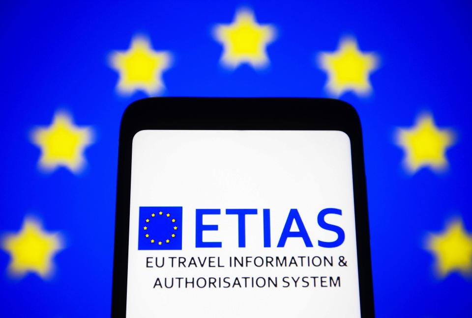 Smartphone displaying the ETIAS logo against a blurred EU flag background.