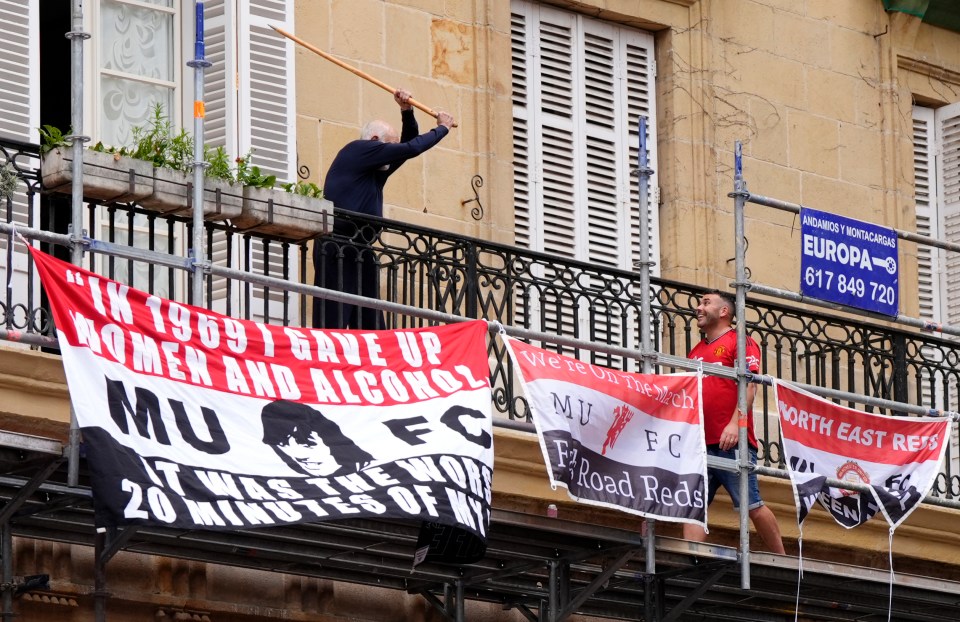A man on a balcony threatens a Manchester United fan with a stick.