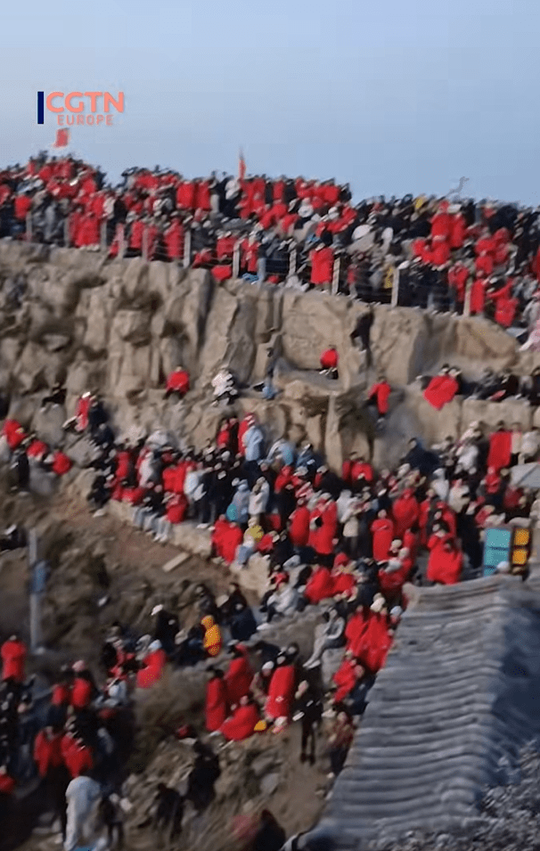 Large crowd of people in red coats gathered on a rocky hillside.