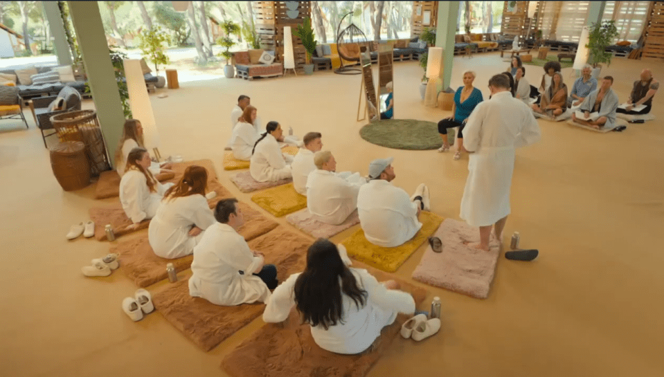 Group of people in white robes sitting on mats in a large room.