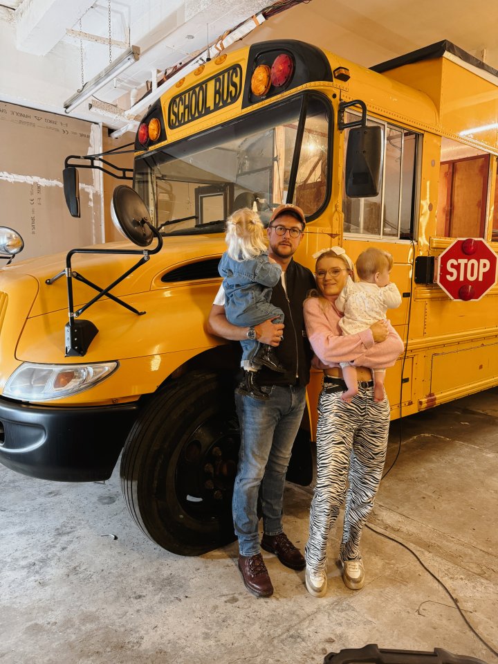 Family with two toddlers standing in front of their renovated school bus.