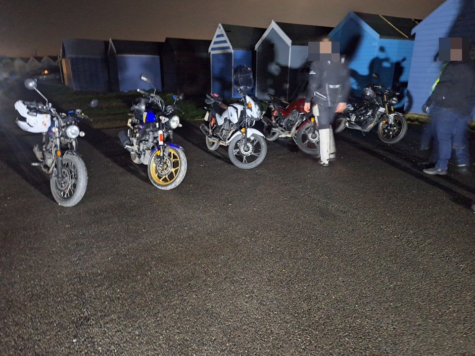 Several motorcycles parked at night near beach huts.