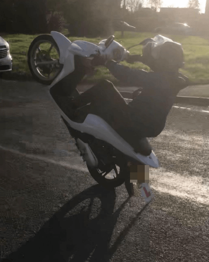 Person doing a wheelie on a white scooter.
