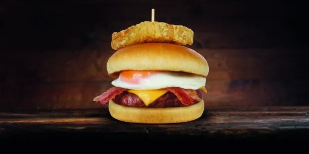 Burger with fried egg, bacon, cheese, and hash brown on top.