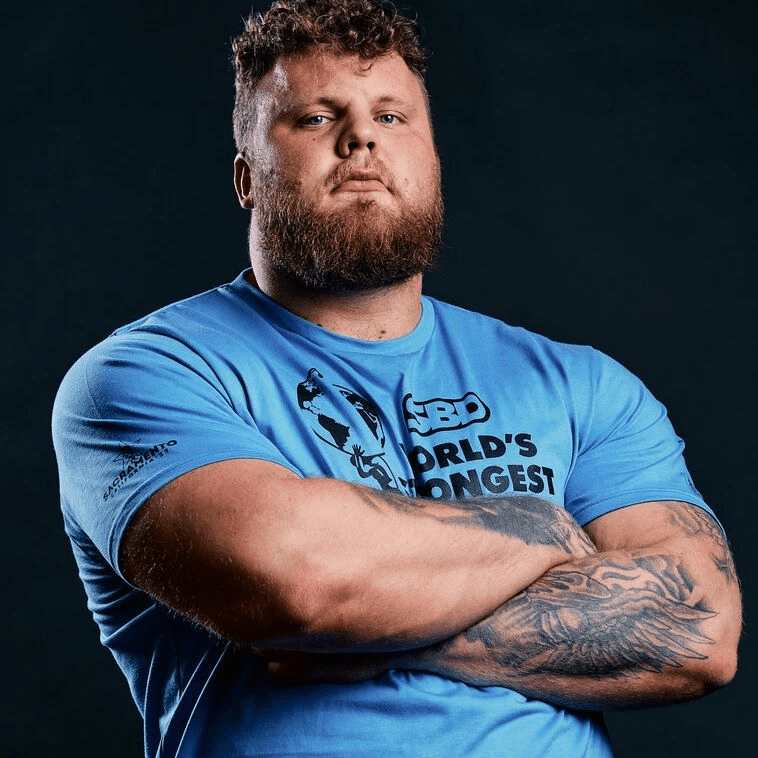 Portrait of a strongman with arms crossed, wearing a blue shirt that says "World's Strongest".