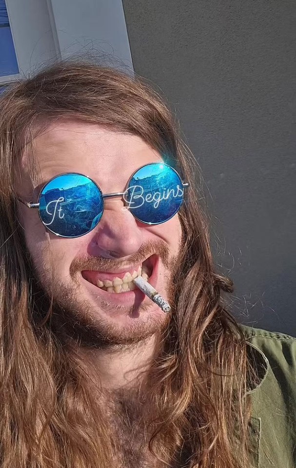 Man with long hair and round sunglasses that say "It Begins" smoking a cigarette.