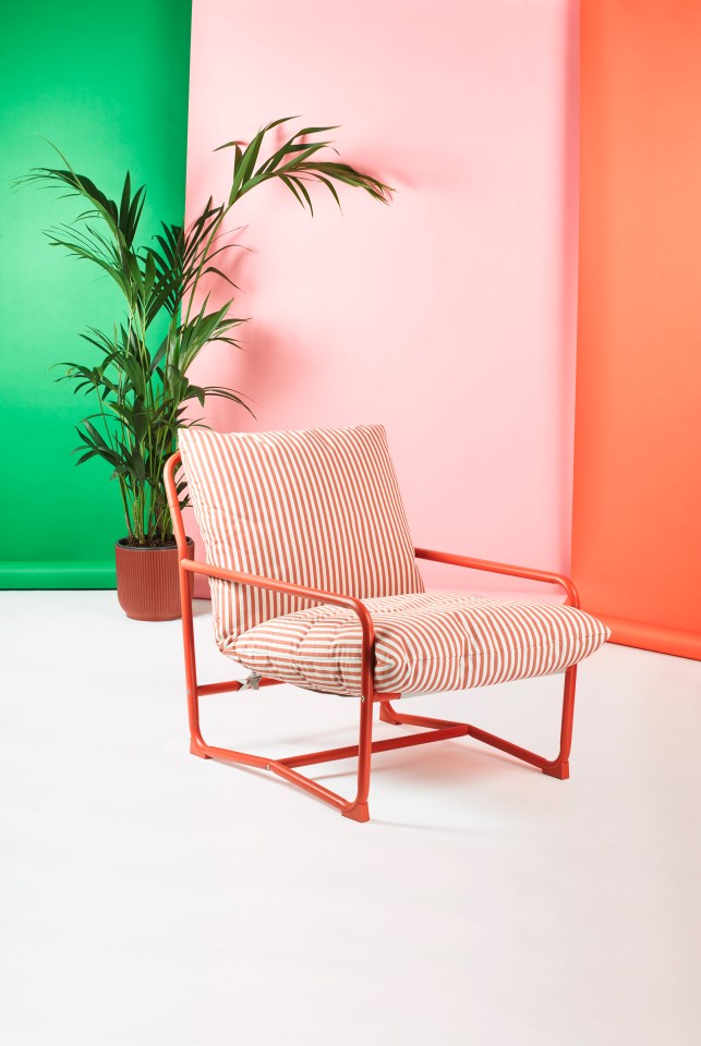 Red metal chair with striped cushions in front of a pink, green, and orange background.