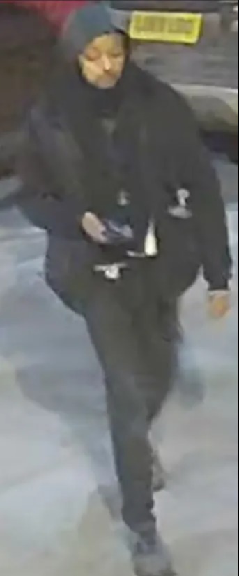 Surveillance image of a person wearing dark clothing and a hood.