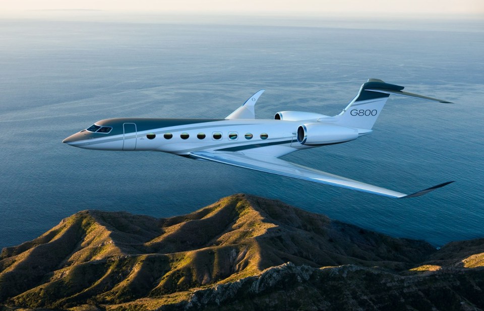 Gulfstream G800 private jet in flight over ocean and hills.