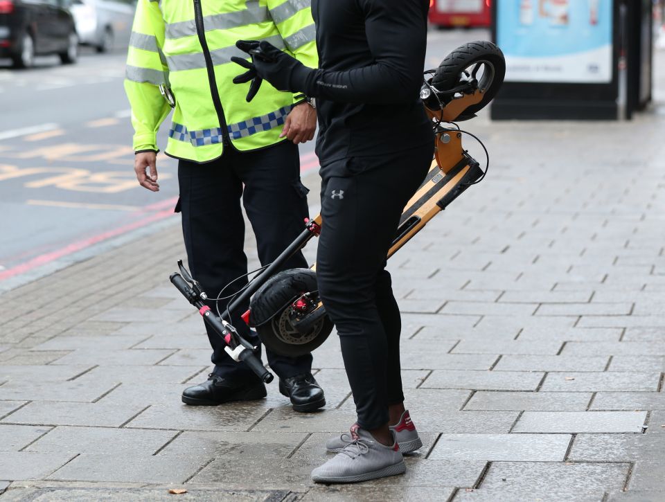 A police officer speaking to a person holding an e-scooter.