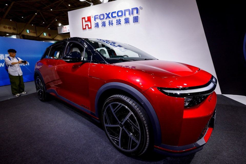 Person photographing a red Foxconn car on display.