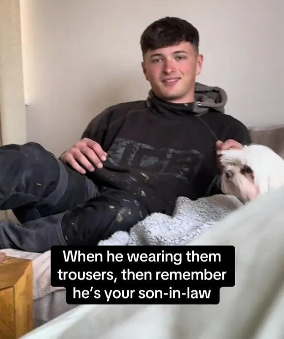Man petting a small white dog while wearing work trousers.