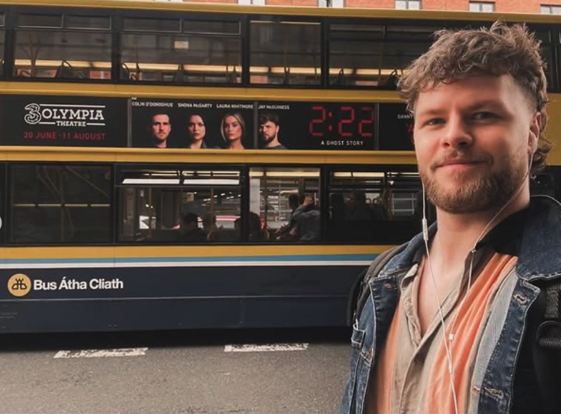 Man standing in front of a bus with a 2:22 A Ghost Story advertisement.