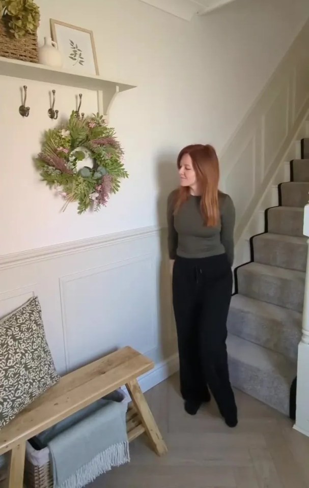 Woman standing in hallway with DIY paneling, wreath, and bench.