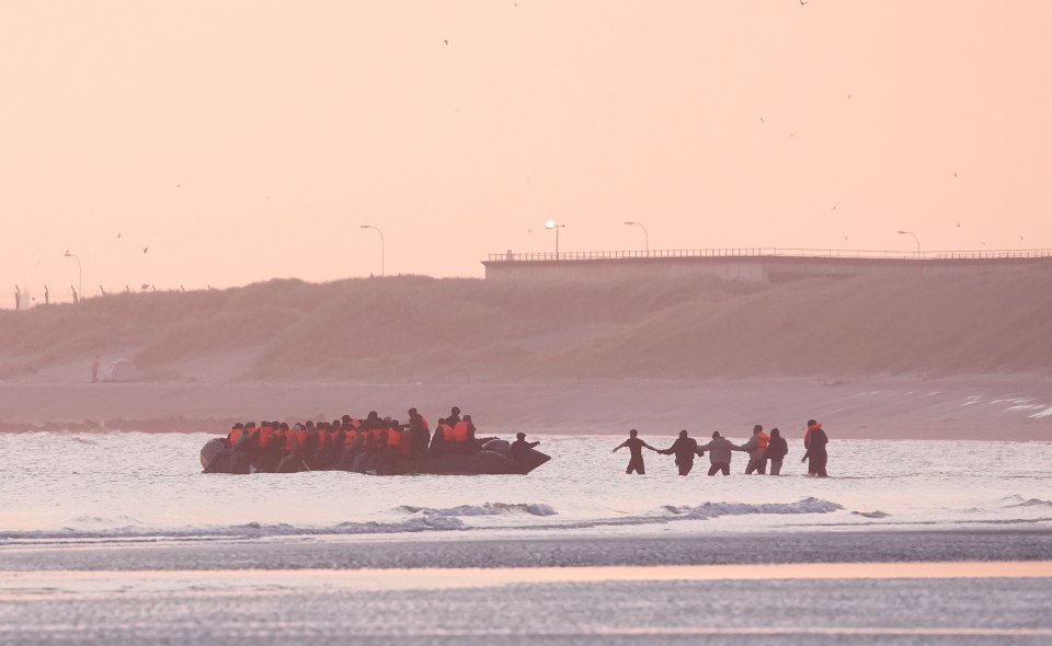 Migrants in a small boat leaving a beach.