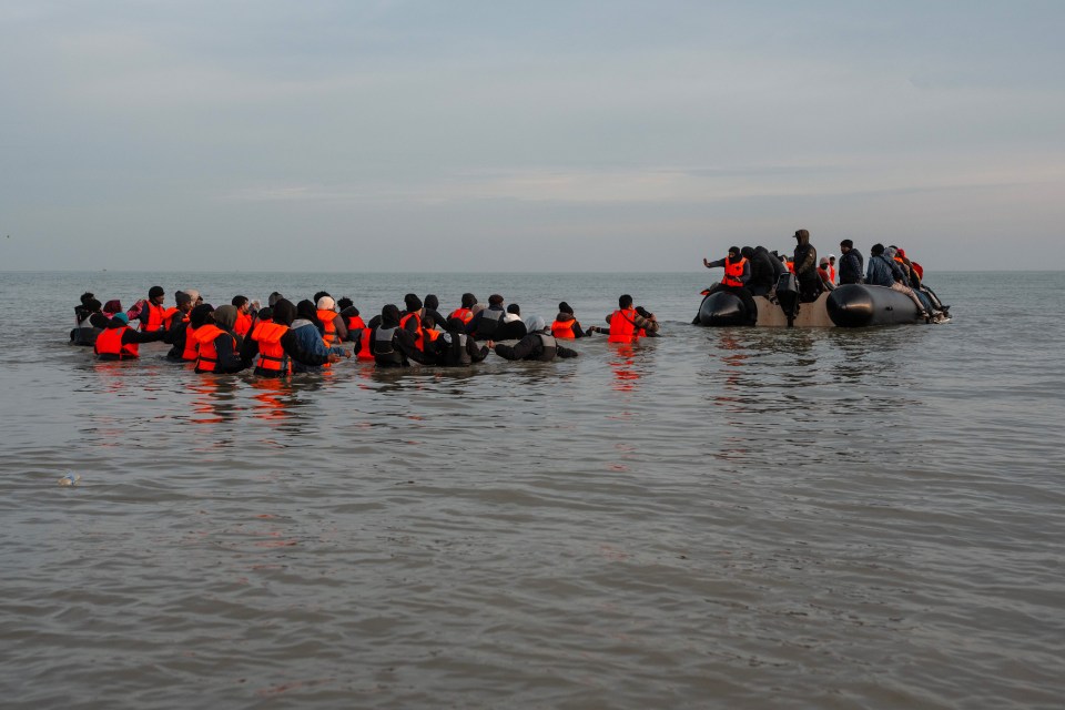 Migrants in life vests entering a small boat in the water.