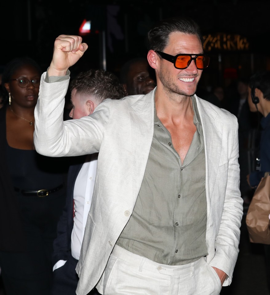 Man in light suit and orange sunglasses raises his fist.
