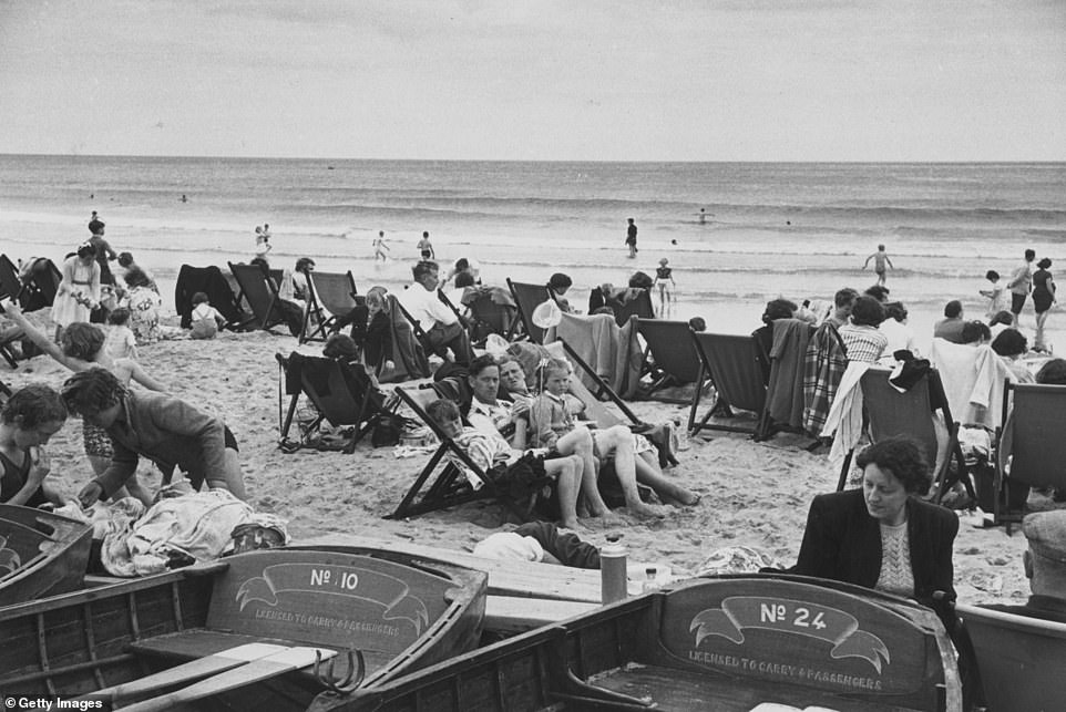 Tourists are seen on Bournemouth Beach in 1954 during what the photographer describes as 'bracing weather' in August