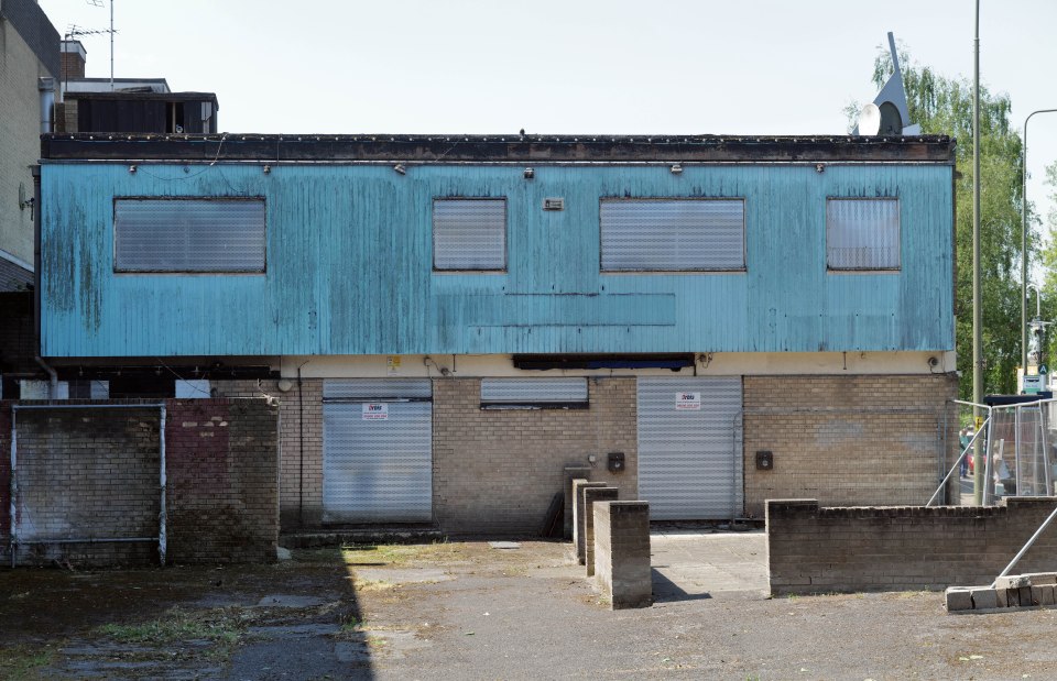 A derelict building with teal siding and roll-down security gates.