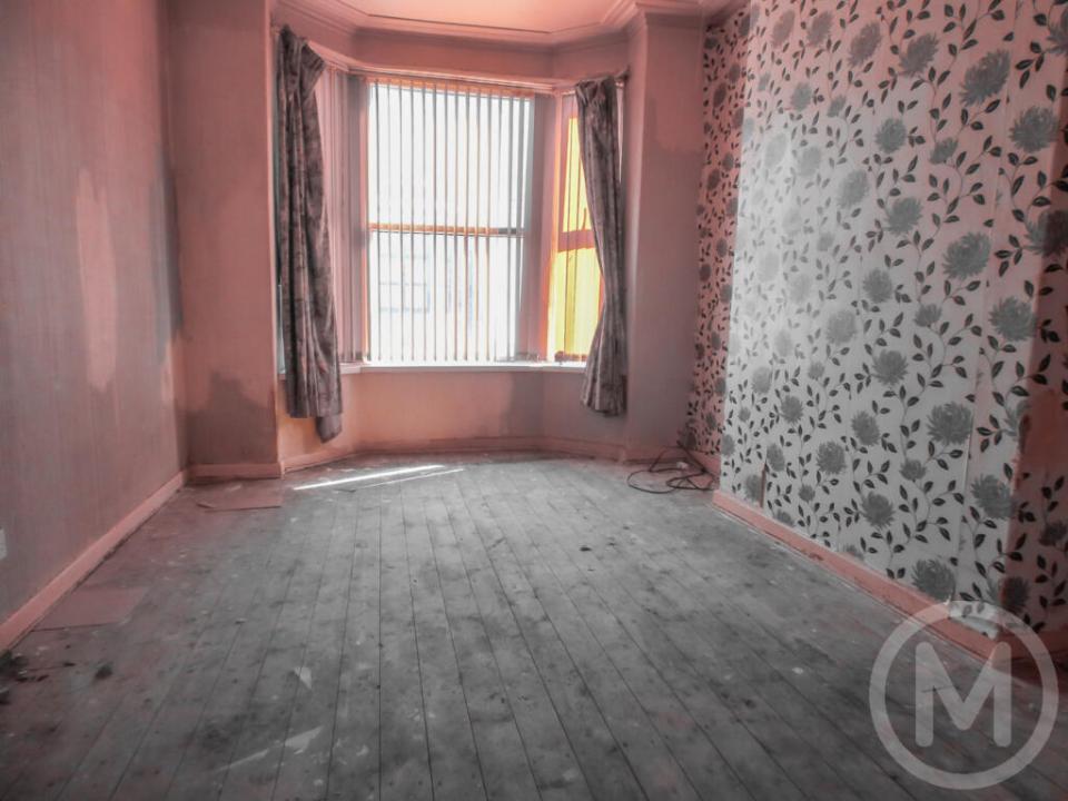 Empty room with damaged wood floors and floral wallpaper.