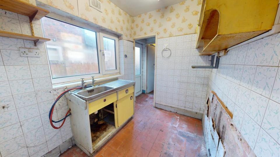 A dilapidated kitchen with yellow cabinets and damaged tiling.