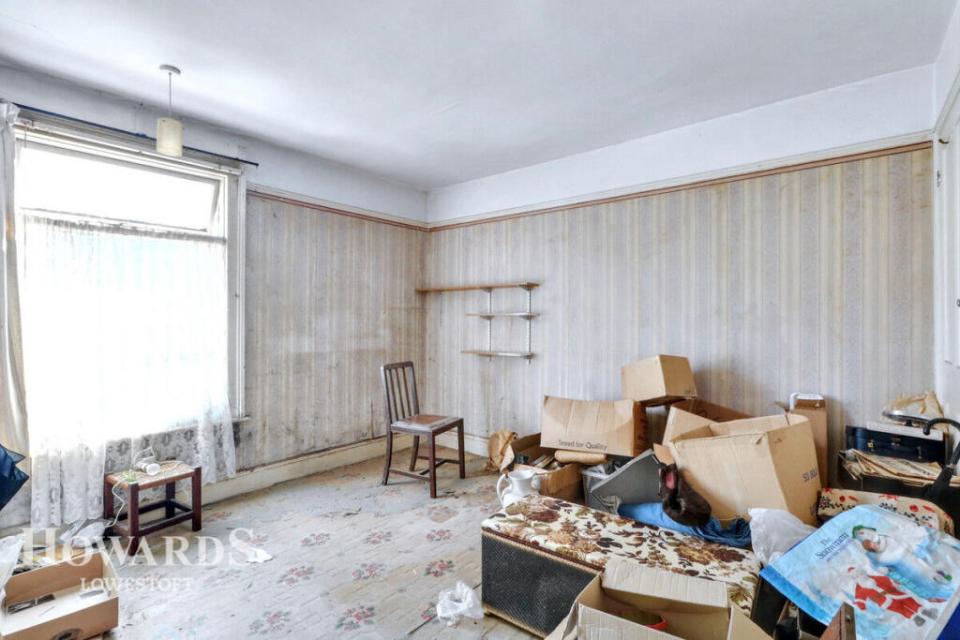 Empty room with damaged walls, boxes, and old furniture.