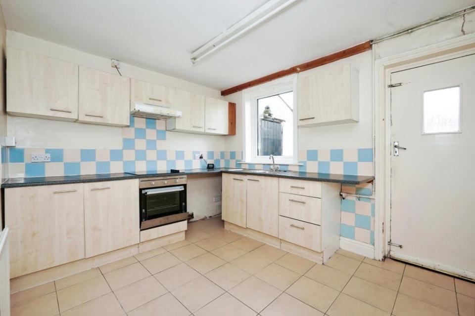 Empty kitchen with light wood cabinets and blue and beige checkered tile backsplash.