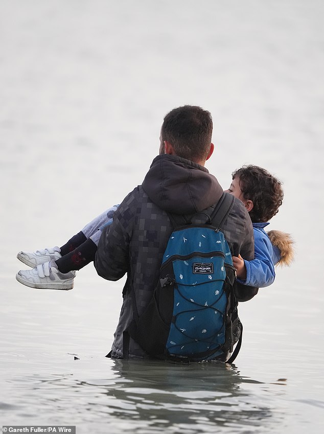 A man carries a young child to a small boat off the coast of France in a bid to reach the UK by crossing the Channel