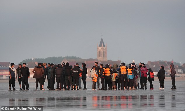 A group of people including women and young children are seen waiting to try and catch a boat to the UK on Saturday at Gravelines in France
