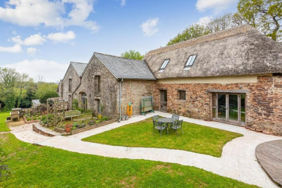 Stone barn with thatch roof and garden.