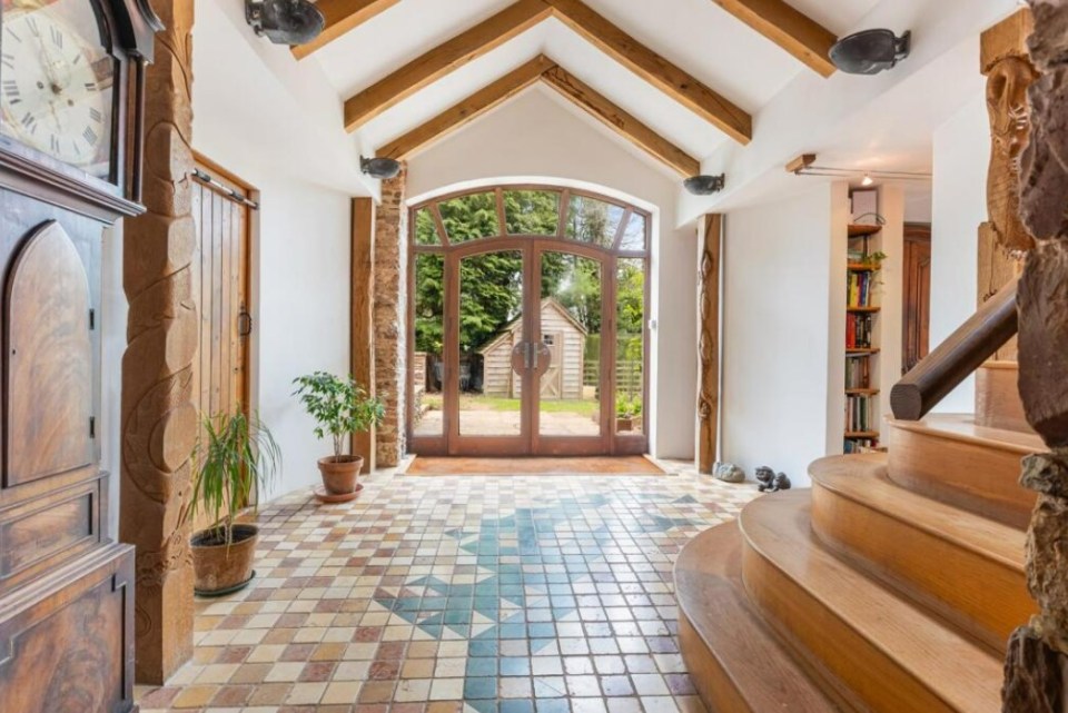 Interior view of a barn conversion hallway with patterned tile floor, wooden staircase, and French doors opening to a garden.