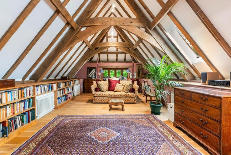 Interior view of a large attic room with exposed wooden beams, a sofa, built-in bookshelves, and an antique dresser.
